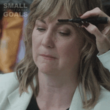 a woman is getting her eyebrows trimmed with a small achievable goals ad in the background