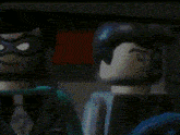 a close up of two lego superheroes , batman and superman , standing next to each other in a dark room .