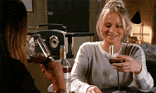 two women are sitting at a table holding wine glasses and smiling .