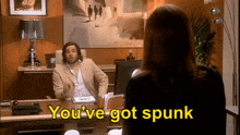 a man in a suit is sitting at a desk talking to a woman who says you 've got spunk .