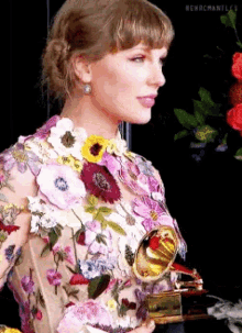 taylor swift is holding a grammy award in a floral dress .