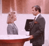 a man in a suit and tie is standing next to a woman in a suit and talking to her .