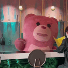 a large pink teddy bear is sitting at a table
