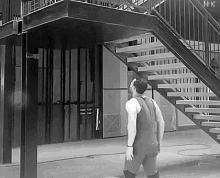 a black and white photo of a man standing in front of a set of stairs with hk written on the bottom right