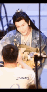 a man in a traditional costume is holding a bouquet of flowers while talking to another man .