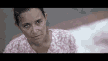 a woman in a pink floral shirt is looking at the camera with a serious look on her face .