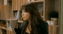 a woman is drinking a cup of coffee in front of a wooden bookshelf .