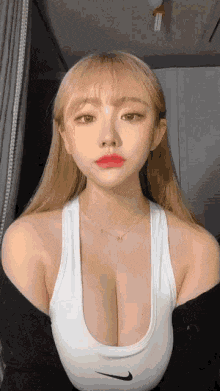a woman in a white tank top with a very plunging neckline is looking at the camera .