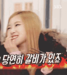 a woman with blonde hair is smiling and holding chopsticks in front of a sign that says ' sbs ' on it