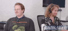 two men are sitting next to each other in an office wearing headphones and glasses .