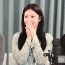 a woman is sitting in front of a microphone with her hands on her face .