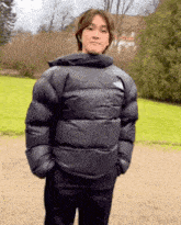 a man wearing a black north face jacket is standing in front of a grassy field