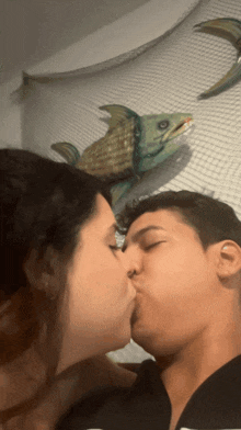 a man and a woman are kissing in front of a fish on a wall