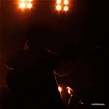 a man in a hat is playing a guitar in a dark room with lights behind him