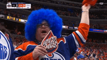 a man wearing a blue wig holds a sign that says lets go oilers