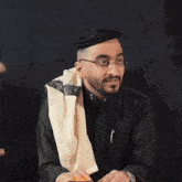 two men are standing next to each other and one is wearing glasses and a towel around his neck .