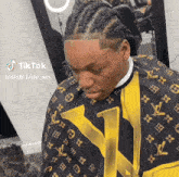 a man wearing a yellow and black louis vuitton cape is getting his hair cut