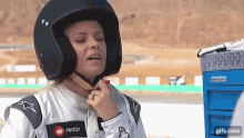 a woman wearing a helmet and racing suit is adjusting her helmet .