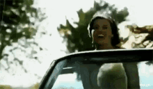 a woman is laughing while driving a car with a man in the back seat .