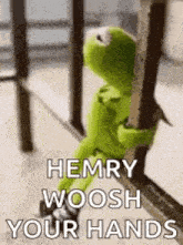 kermit the frog is sitting on a railing holding onto a pole .