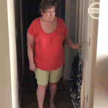 a woman in a red shirt and green shorts is standing in a hallway next to a sign that says pets