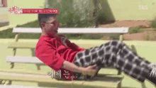 a man in a red shirt is laying on a bench .