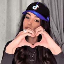 a woman wearing a blue hat with the letter t on it makes a heart shape with her hands