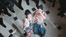 a group of people are standing around two girls one of whom is wearing a crop top with a teddy bear on it