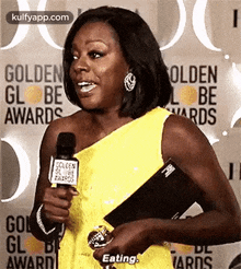 a woman in a yellow dress is holding a microphone and talking into it at the golden globe awards .
