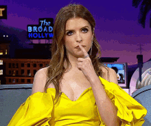 a woman in a yellow dress is sitting in front of a broad hollywood sign
