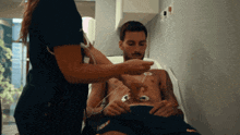 a shirtless man is being examined by a nurse who is wearing a nike shirt