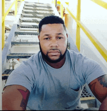 a man with a beard wearing a grey shirt is sitting on stairs
