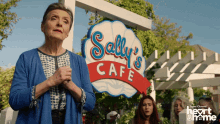 an elderly woman stands in front of a sign for sally 's cafe
