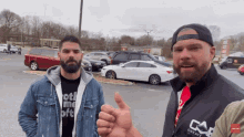 two men are standing in a parking lot and one of them is wearing a shirt that says " not me "