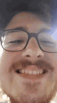 a man with glasses and a beard is smiling and making a funny face .