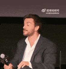 a man in a suit and white shirt is holding a microphone in front of a screen with chinese writing on it