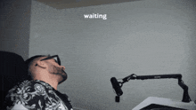 a man is laying in front of a microphone with the word waiting behind him