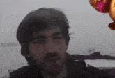 a man with a beard is looking at the camera with a pink balloon in the background