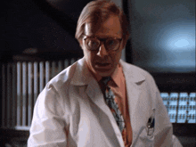 a man wearing glasses and a white lab coat stands in front of a computer monitor
