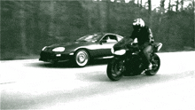 a black and white photo of a man on a motorcycle and a car
