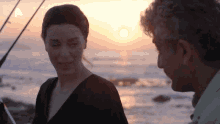a man and a woman are standing on a beach at sunset with the letter a on the bottom left