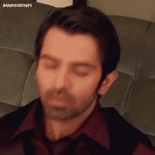 a man is sitting on a couch with his eyes closed and his mouth open .