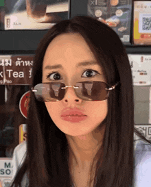 a woman wearing sunglasses stands in front of a tea sign