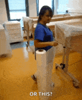 a woman in a blue scrub is holding a roll of toilet paper in a hospital room and asking " or this "