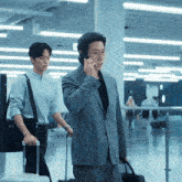 a man in a suit is talking on a cell phone while another man pushes a suitcase