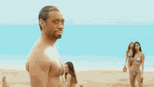 a group of women in bikinis are standing on a beach with a shirtless man in the foreground .