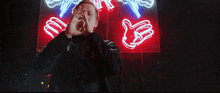 a man wearing a black hoodie with the word army on it stands in front of a neon sign