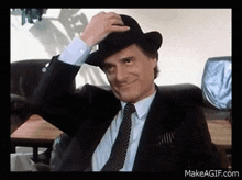 a man in a suit and tie is adjusting his hat while sitting in a chair .