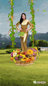 a woman in a gold dress is standing next to a basket of flowers on a swing