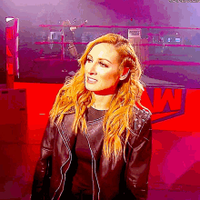 a woman in a black leather jacket is standing in front of a wrestling ring